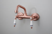 Koperkleurige landelijke muurkraan met keramische handgrepen